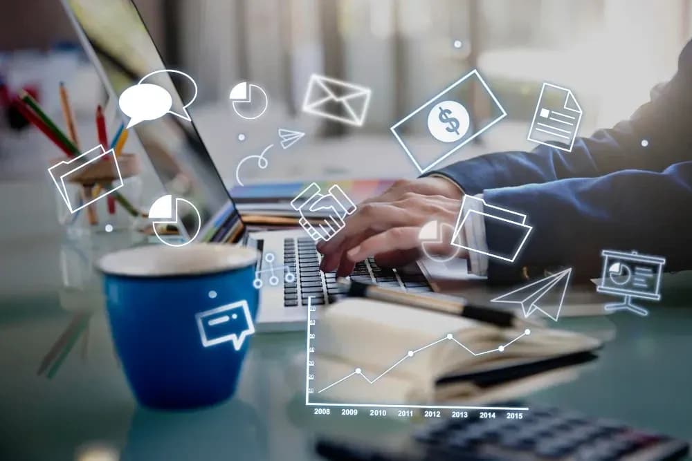 Hands typing on a laptop surrounded by digital icons representing business, communication, finance, and data analysis, with a coffee mug and notebook on the desk.